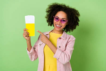Portrait of attractive cheerful girl indicate finger flight tickets passport isolated on green color backgroundの写真素材