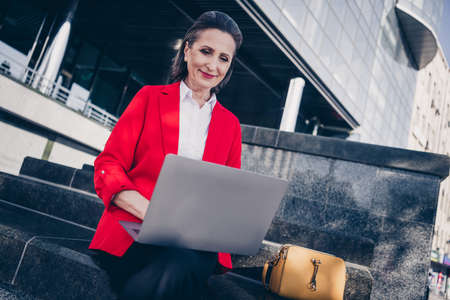 Photo of executive fashionable aged lady sit stairs financial modern center use netboook texting partners outdoorsの写真素材