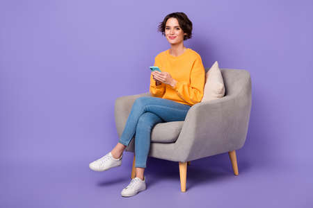 Full size portrait of positive nice person sit chair hold use telephone gadget isolated on purple color backgroundの写真素材