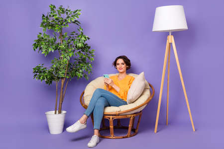 Portrait of attractive cheery girl sitting in chair using device rest free spare time isolated over violet lilac color backgroundの写真素材