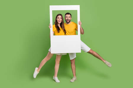 Full length portrait of two excited positive people arms hold paper album card isolated on green color backgroundの写真素材