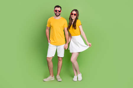 Full size portrait of two positive cheerful partners hold arms enjoy weekend isolated on green color backgroundの写真素材