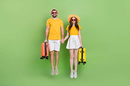 Full body portrait of two active overjoyed partners hold arms jumping isolated on green color backgroundの写真素材