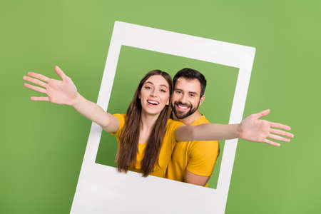 Portrait of two excited positive people raise arms through paper window isolated on green color backgroundの写真素材