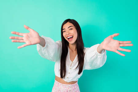 Portrait of excited friendly thai girl raise opened arms welcome invite you isolated on shine aquamarine color backgroundの写真素材