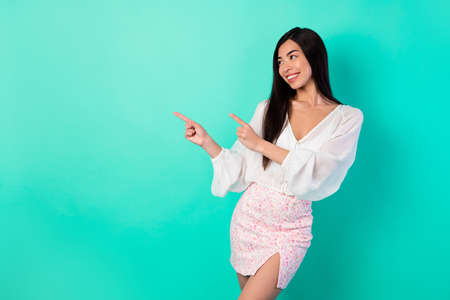Portrait of cheerful pretty indonesian lady look indicate fingers empty space blank isolated on vibrant cyan color backgroundの写真素材