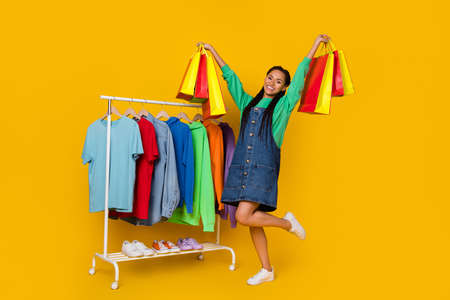 Full length photo of overjoyed attractive lady hands hold raise packages isolated on yellow color...