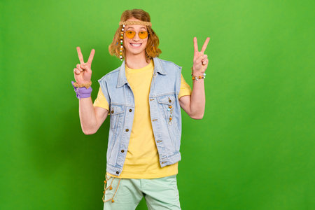 Portrait of attractive cheerful funny carefree guy hippie showing double v sign isolated over bright green color backgroundの写真素材