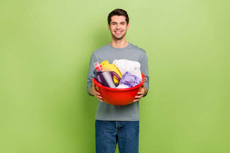 Photo of good mood cheerful man doing household chores cleaning dirty clothes isolated on green color backgroundの写真素材