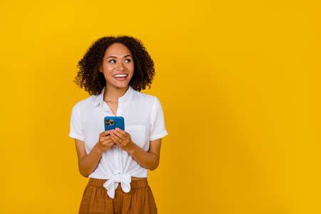 Portrait of charming minded girl hold telephone look empty space isolated on yellow color background