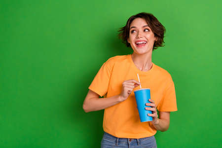Photo of sweet dreamy young lady wear orange outfit drinking soda looking empty space isolated green...