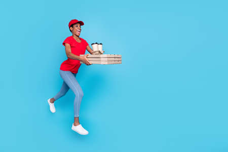 Photo of positive short hair human wear red uniform jumping high delivering fast food empty space isolated blue color backgroundの写真素材