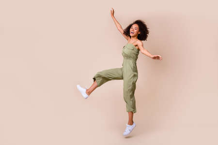 Full length photo of attractive young girl curly hair jumping carefree have fun wear trendy khaki outfit isolated on beige color backgroundの写真素材
