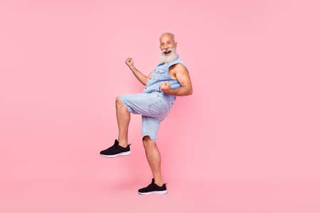 Full length photo of funny lucky retired guy wear jeans waistcoat walking rising fists isolated pink color backgroundの写真素材