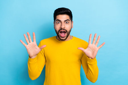 Photo of impressed funny man wear yellow sweater rising arms isolated blue color backgroundの写真素材