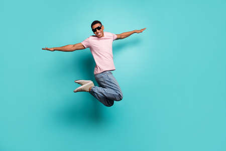 Full length photo of pretty childish guy wear pink t-shirt jumping high arms sides empty space isolated teal color backgroundの写真素材