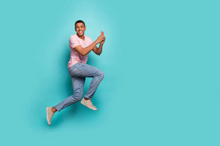 Full length photo of positive sweet guy wear pink t-shirt jumping chatting modern gadget empty space isolated teal color backgroundの写真素材