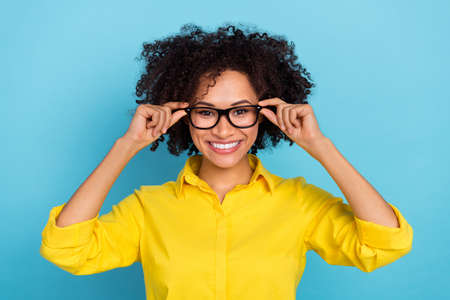 Photo of clever curly hairdo young lady wear yellow blouse eyewear isolated on blue color backgroundの写真素材
