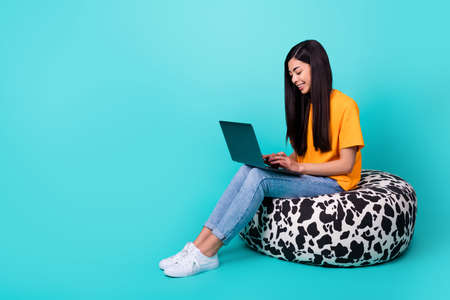 Full length profile photo of ceo brunette lady type laptop sit on bag wear t-shirt jeans shoes isolated on teal backgroundの写真素材