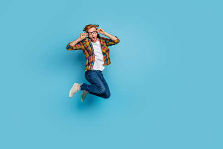 Photo of impressed excited guy with red hairstyle dressed plaid shirt holding glasses jumping...