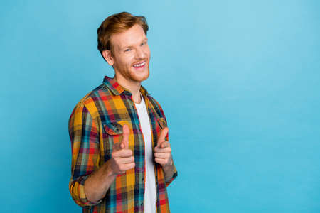 Photo of young handsome good mood man with red hair dressed plaid shirt indicating fingers on camera isolated on blue color backgroundの写真素材