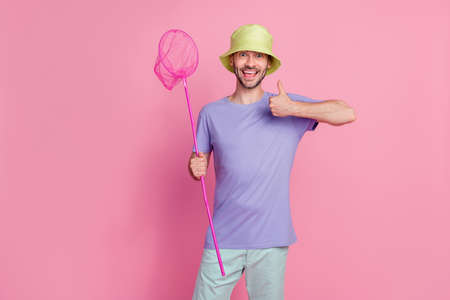 Photo of satisfied joyful guy hold net raise arm show super symbol have fun summer relax rest isolated on pink color backgroundの写真素材
