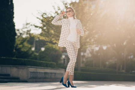 Photo of charming pretty senior lady dressed checkered blazer dark eyewear enjoying sunny weather outdoors urban town streetの写真素材