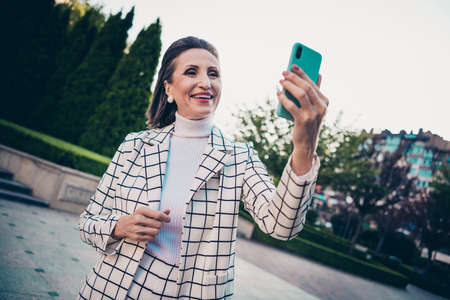 Photo of positive cute woman wear plaid jacket recording self video modern device outside city residential complexの写真素材
