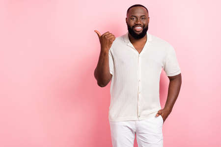 Photo of cute pretty guy dressed white shirt pointing thumb empty space isolated pink color backgroundの写真素材