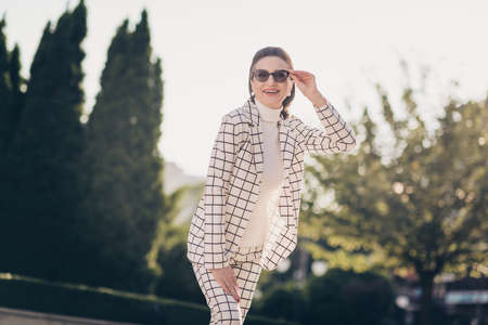 Photo of sweet charming senior lady dressed checkered blazer dark eyewear walking sunny weather outdoors urban town streetの写真素材