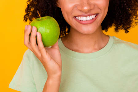 Photo of cute funny lady wear green t-shirt rising apple smiling white teeth isolated yellow color backgroundの写真素材
