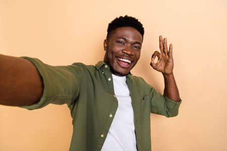 Photo of guy shoot record selfie video make okay symbol wear stylish khaki shirt isolated pastel color backgroundの写真素材