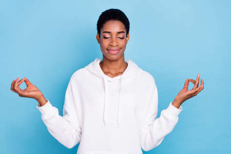 Photo of beautiful attractive unisex lady dressed white hoodie closed eyes practicing yoga isolated blue color backgroundの写真素材