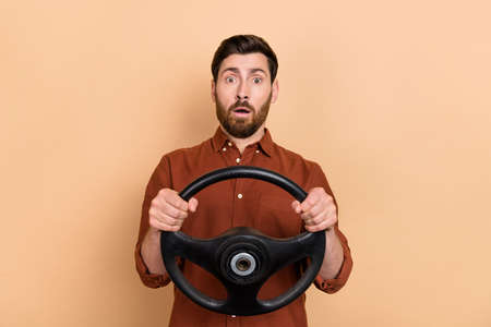 Photo of impressed speechless person hands hold wheel stare cant believe isolated on beige color backgroundの写真素材