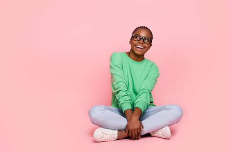 Full length photo of minded cheerful girl sit floor look interested empty space isolated on pink color backgroundの写真素材