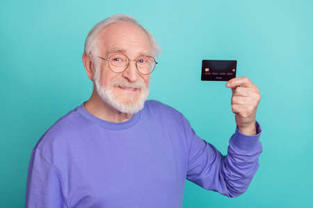 Portrait of friendly satisfied aged man hand hold plastic debit card toothy smile isolated on teal color backgroundの写真素材