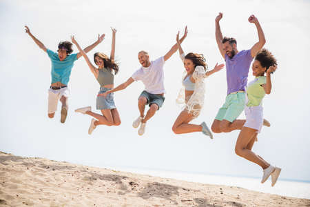 Full length photo of group excited overjoyed carefree buddies jumping enjoy sunny weather sand beach chill outsideの写真素材