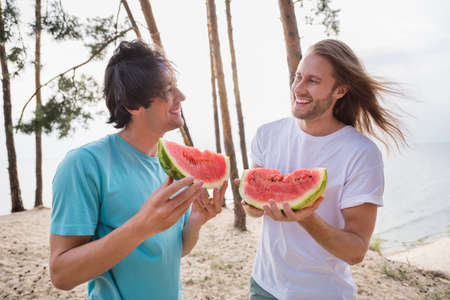 Photo of funky guys eat watermelon wear casual cloth outside on the beach near treesの写真素材