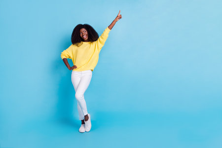 Full size body photo of young happy dancing lady finger pointing looking empty space isolated on blue color backgroundの写真素材
