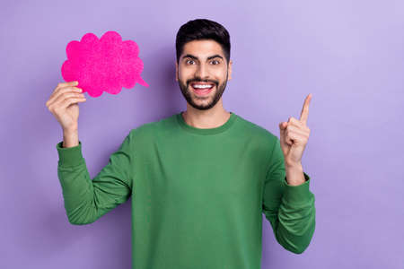 Photo of cheerful young latin arabian man hold paper cloud point empty space wear trendy green clothes isolated on purple color backgroundの写真素材