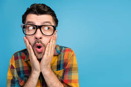 Photo of speechless handsome excited guy in eyewear dressed plaid shirt look empty space shocked sale isolated on blue color backgroundの写真素材