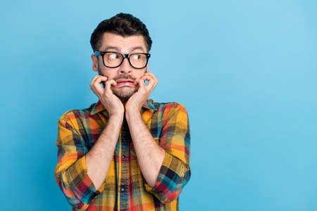 Photo of terrified handsome bearded man wear glasses plaid shirt hands on cheekbones look empty space isolated on blue color backgroundの写真素材