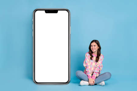 Full body photo of young lovely girl sit floor curious dream look empty space isolated over blue color backgroundの写真素材