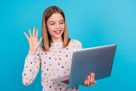 Photo of pretty excited small girl wear dotted shirt waving arm hi modern device isolated blue color...