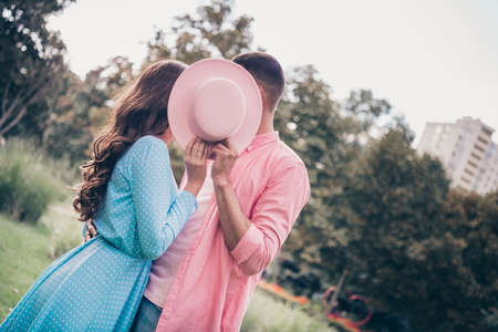 Closeup photo session of two young students boyfriend girlfriend hiding kissing cover pink hat wear stylish clothes in parkの写真素材