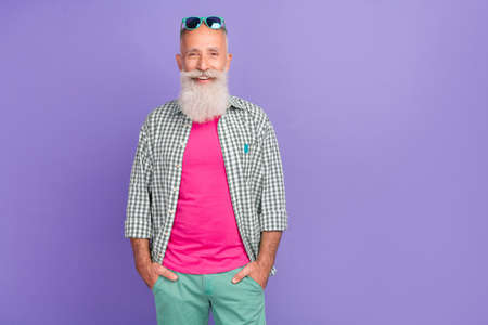 Portrait of satisfied glad aged person put hands pockets toothy smile empty space isolated on purple...