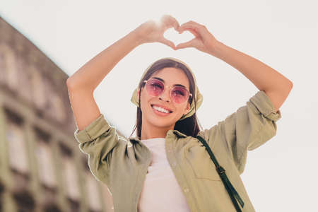 Portrait of charming positive girl hands fingers showing heart gesture above head enjoy warm sunny weather outsideの写真素材