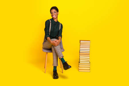 Full length body size view of attractive cheery woman sitting reading materials isolated over bright yellow color backgroundの写真素材