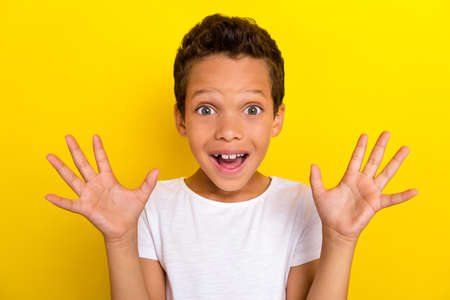 Photo of pretty positive cheerful boy wear white stylish outfit relax rest rejoice show arm palm surprise isolated on yellow color backgroundの写真素材