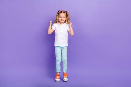 Full length photo of cute small girl tails raise fists jump win competition wear stylish white...
